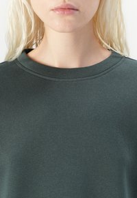 Dark green sweatshirt with a crew neck, made of smooth fabric, featuring subtle stitching details and a relaxed fit.