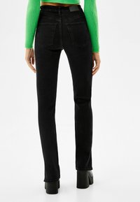 Svarta raka jeans med medelhög midja, femfickorsdesign och framträdande bakfickor, parat med plattformsklackar.