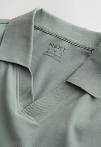 Lysegrøn polo-shirt med et blødt, tekstureret stof. Har en V-halskrave og syede detaljer. Mærketiketten er synlig indeni kraven.