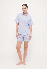 Camisa de manga corta azul claro y pantalones cortos a juego, con un patrón a rayas y pequeños motivos de corazones azules. Material de algodón.