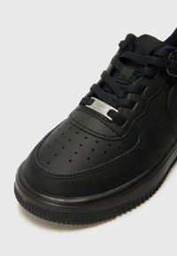 Svarte lærersneakers med jevn tekstur, perforert tåboks, svarte snørebånd og en sølvfarge på tungen. Tykk gummisåle.