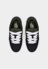 Paire de baskets Vans noires et vert foncé avec lacets blancs et semelles épaisses blanches, vues de dessus sur un fond uni.
