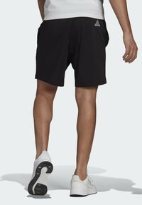 Shorts deportivos negros con cinturilla elástica y bolsillos laterales, combinados con zapatillas blancas que tienen una suela texturizada y detalles de logotipo.