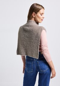 Pull en maille gris cropped avec un col montant, doté d'une finition douce et texturée. Porté par-dessus un haut à manches longues rose clair et un jean bleu.