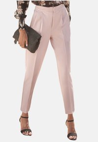 Lichtroze op maat gemaakte broek met plooien, ontworpen voor een getailleerde look. Gecombineerd met een gestructureerde zwarte clutch en zwarte hakken.