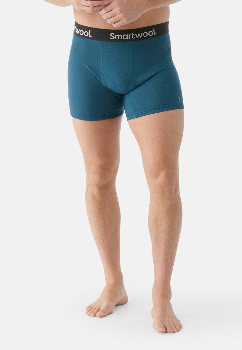 Boxer briefs Smartwool di colore teal con una vita nera e logo, design aderente, texture liscia e lunghezza fino a metà coscia.