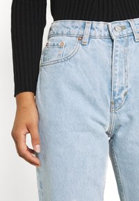 Jeans in denim azzurro chiaro con vita alta, taglio dritto e cuciture visibili. Presentano quattro tasche e dettagli in metallo color rame.