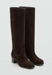 Brązowe zamszowe kozaki za kolano o zaokrąglonym nosku, z delikatnym przeszyciem dekoracyjnym i obcasem typu blok. Gładka podszewka wewnętrzna i czysta sylwetka.