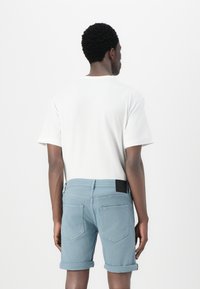 Hvid t-shirt med korte ærmer, parret med lyseblå denimshorts, der har rullede kanter og to baglommer. Sort mærke på linningen.