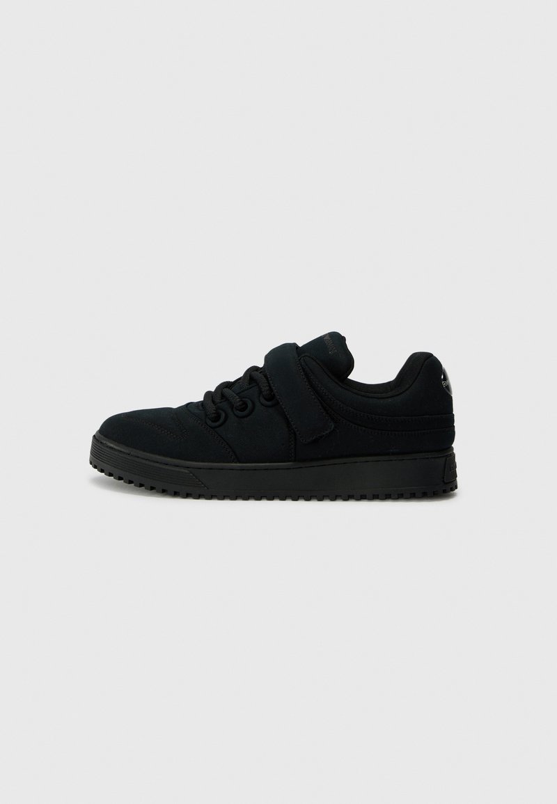 Black sneakers with a smooth textured upper, rounded toe, lace-up design, and adjustable strap. Thick rubber sole with traction pattern.