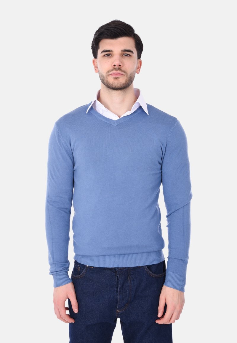 Maglione blu lavorato a maglia con scollo a V, maniche lunghe e polsini a coste. Indossato sopra una camicia bianca con colletto, abbinato a jeans in denim scuri.
