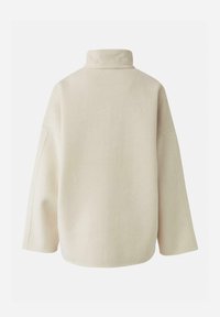 Pull beige surdimensionné avec un col montant, des épaules tombantes et un tissu doux et texturé. Le dos présente un design simple et épuré.