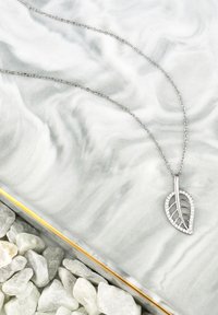 Silver halsband med ett bladformat hänge, med utskurna detaljer och små strassackenter, hängande på en delikat kedja.
