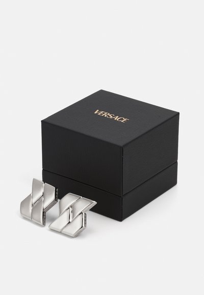 Silver metal cufflinks with a geometric design, displayed beside a black textured box featuring gold "Versace" logo on the lid.