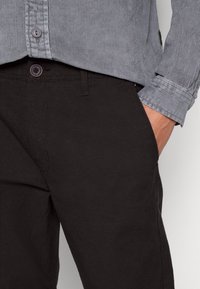 Gray corduroy button-up shirt with subtle ribbing, paired with black textured pants. Features a front pocket and button detail.