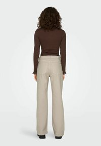 Vaaleanbeiget leveälahkeiset housut, joissa on sileä pinta ja kaksi takataskua, yhdistettynä istuvaan ruskeaan pitkähihainen yläosaan.