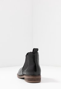 Černá kotníková bota z kůže s hladkým a strukturovaným povrchem, elastickými bočními panely a nízkým dřevěným podpatkem.