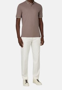 Hnědý polo tričko s bílým a šedým pruhovaným límečkem, spárované s bílými kalhotami a béžovými teniskami. Hladká tkanina s přiléhavým střihem.