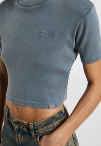 T-shirt cropped a maniche corte in morbido tessuto a coste blu chiaro con logo ricamato. Abbinato a pantaloni shorts in denim a vita alta con un motivo sbiadito.