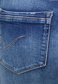 Kulumise märgiga siniste teksade tagatasku, millel on kollane õmblus ja kaarjas dekoratiivõmblus.