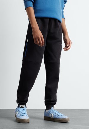 Pantaloni sportivi neri con un fit affusolato, tasche laterali con zip e un finish testurizzato, abbinati a sneakers basse azzurre con dettagli a stella.