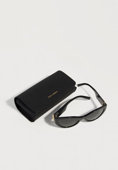 Μαύρα γυαλιά ηλίου σε σχήμα cat-eye με σκούρους φακούς, δίπλα σε μαύρη υφασμάτινη θήκη με χρυσό λογότυπο Dolce & Gabbana πάνω σε λευκή επιφάνεια.
