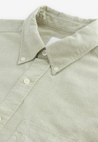 Chemise vert clair boutonnée avec col et boutons blancs, en tissu texturé.