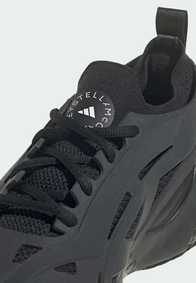 Chaussure de sport noire avec une tige en maille, un bout arrondi, un laçage prononcé et une semelle intermédiaire texturée avec un logo sur la languette.