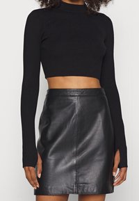 Top corto nero a coste con maniche lunghe e scollatura alta abbinato a una gonna in pelle nera caratterizzata da una consistenza liscia e uno spacco laterale.