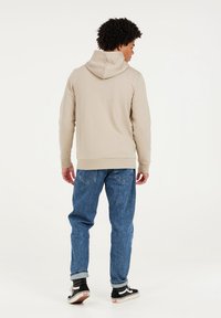 Beige Hoodie mit Kordelzugkapuze, weicher Textur, gerippten Bündchen und Saum, kombiniert mit blauen Jeans und schwarzen Sneakers.