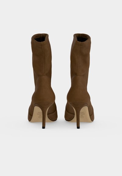 Paire de bottines en suède marron à talons hauts, vues de dos avec des talons aiguilles fins et des détails de coutures courbées.