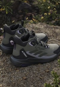 Green and black hiking shoes with textured fabric, high ankle support, reinforced sole, and purple accents. Lightweight design for outdoor use.