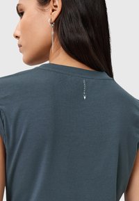 Mørk teal T-shirt med korte ærmer, glat tekstur og en lille logodetalje nær halsen på ryggen.