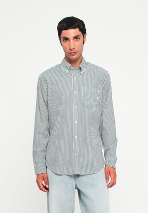 Cotton long-sleeve shirt with a green and white vertical striped pattern, buttoned collar, and front pocket. Paired with light blue denim pants.