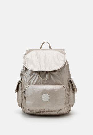 Zaino metallico beige con chiusura a patta, maniglia superiore, tasca frontale con cerniera e tasche laterali. Presenta un logo circolare sul davanti.