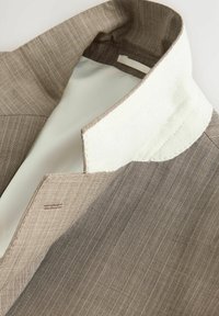 Colletto di giacca a motivo chevron marrone con fodera interna chiara e dettagli cuciti. Presenta un morbido accento di colletto in feltro bianco.