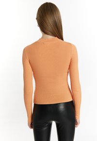 Top a maniche lunghe a coste di colore arancione chiaro, design aderente con scollo a girocollo. Abbinato a leggings neri lucidi a vita alta.