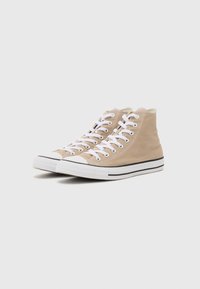 Beige High-Top-Canvas-Sneaker mit weißen Schnürsenkeln, schwarzem Streifen am Sohlenrand und Gummikappen. Klassisches Design und strukturierte Oberfläche.