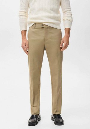 Beige tailored trousers with a flat front, straight leg, and subtle crease detail. Paired with black loafers and a cream sweater.