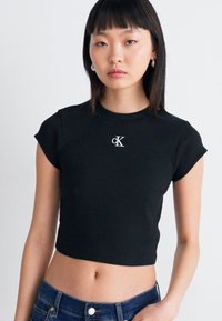 T-shirt noir court à manches courtes, avec un petit logo blanc "cK" sur la poitrine. Fabriqué en tissu côtelé avec un design ajusté.