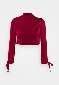 Červený saténový crop top s vysokým výstřihem, dlouhými rukávy a uvázanými manžetami. Hladký povrch s přiléhavým střihem a mírným nařasením na ramenech.