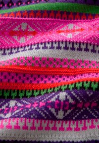 Tifă colorată tricotată cu modele geometrice în nuanțe de roz, violet, verde și gri. Suprafață texturată cu lățimi și forme variate ale liniilor.