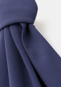 Tissu bleu foncé torsadé en nœud, montrant un tissage texturé et des plis lisses sur un fond clair.
