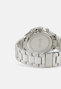 Orologio in metallo argentato con bracciale in acciaio inossidabile, caratterizzato da una cassa rotonda, quadranti cronografi e una finitura lucida. Retro contrassegnato "BOSS."