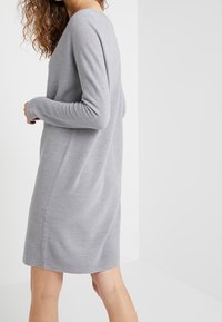 Robe grise en tricot à manches longues, avec une coupe décontractée et une texture lisse. Légèrement plus longue à l'arrière, présentant des lignes épurées.