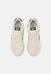 Beige athletic shoes with a mesh upper, textured accents, flat laces, and a padded collar, featuring a logo on the tongue.