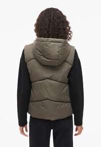 Maslinasto zelena prsluk na preklop s visokim ovratnikom i kapuljačom, s prošivenim uzorkom i crnim dugim rukavima. Meki materijal, ležerni kroj.