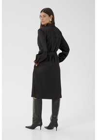 Rochie din satin negru cu mâneci lungi, talie accesorizată cu un brâu și cizme pe toc stiletto negre, până la genunchi. Textură fină, design minimal.
