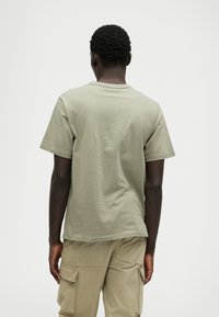 Krótki rękaw, oliwkowa koszulka z miękkiej bawełny, z okrągłym dekoltem i luźnym krojem, połączona z jasnobeżowymi spodniami cargo.