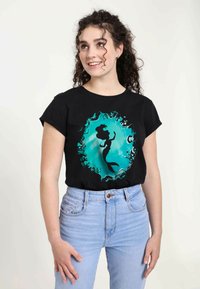 Svart t-shirt med en turkos silhuett av en sjöjungfru omgiven av en abstrakt vågdesign. Korta ärmar, avslappnad passform.
